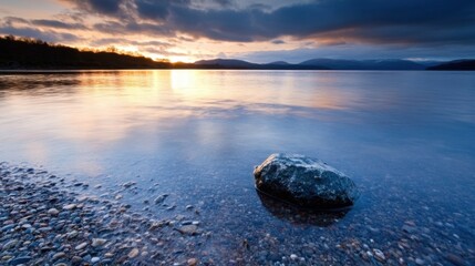 Poster - Serene sunset over a calm loch, single rock in shallow, clear water, pebbles on shoreline, mountains in the distance under a dramatic sky. : Generative AI