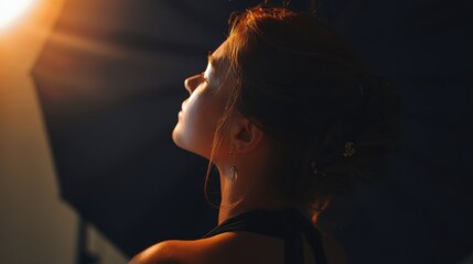 Aufkleber - A young woman with auburn hair, wearing a black dress and delicate earrings, gazes upward, bathed in warm, golden light streaming from above. : Generative AI