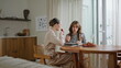© stockbusters - Two ladies discussing fashion style looking magazine on kitchen. Women talking