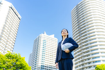 Aufkleber - 新緑の街の前にヘルメットを持って立つ女性ビジネスパーソン