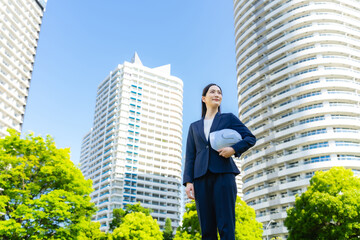 Aufkleber - 新緑の街の前にヘルメットを持って立つ女性ビジネスパーソン