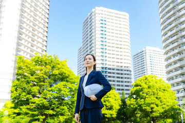 Aufkleber - 新緑の街の前にヘルメットを持って立つ女性ビジネスパーソン