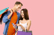 © vgstudio - Image - young happy smile couple. Man carry shop bags. Woman, dress tank top, hold show something on cellphone smartphone mobile phone, isolated rose pink background. Holiday sale ad concept.