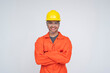 © Mdv Edwards - Young Southeast Asian male construction worker smiling with arms confidently crossed, wearing safety gear and orange coveralls. Isolated on a light background.