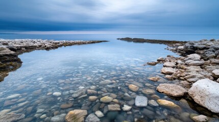 Aufkleber - Serene coastal scene: crystal-clear water reveals smooth, multicolored pebbles lining a rocky shore under a dramatic, cloudy sky. : Generative AI