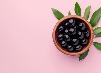 Aufkleber - A wooden bowl filled with glistening black olives sits on a pink background, accented by fresh green olive leaves. : Generative AI