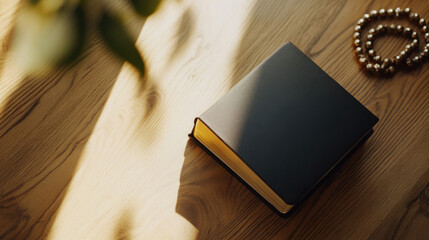 Aufkleber - A dark-blue hardcover book rests on a light-brown wooden table, bathed in sunlight, with gold-toned beads subtly placed nearby. : Generative AI