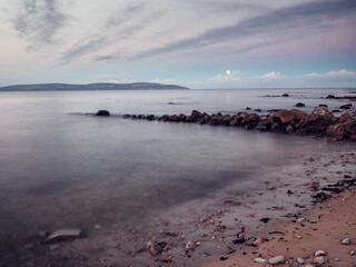 Wall Mural - View on peaceful Galway bay and Burren mountains from rough stone coast. Water surface is smooth and gives relaxing feel and mood. Irish nature landscape scene. Nobody. Cloudy sky.