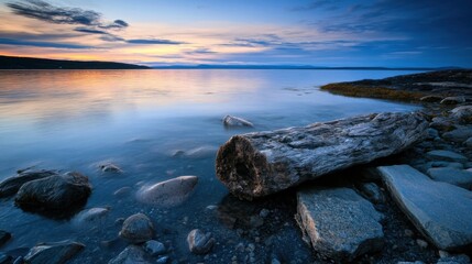 Leinwandbilder - Serene sunset over calm water, a large grey driftwood log rests on smooth, dark rocks near the shoreline.  The sky displays a beautiful blend of orange, pink, and blue hues. : Generative AI