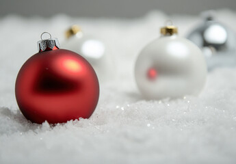 Aufkleber - A single red christmas bauble rests in artificial snow, with blurred white and silver ornaments in the background, creating a festive winter scene. : Generative AI