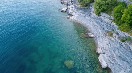 Poster - Aerial view of a tranquil lake meeting a rocky shoreline, showcasing clear turquoise water and layered limestone cliffs with lush green vegetation. : Generative AI