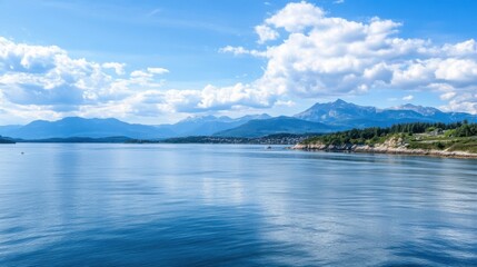 Aufkleber - Serene coastal view of a fjord with mountains under a bright summer sky, featuring calm blue water and a small town nestled along the shoreline. : Generative AI