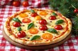 © WoodHunt - A pizza decorated with cherry tomatoes and basil leaves arranged like Christmas ornaments and stars. It's placed on a red and white checkered tablecloth with pine branches nearby