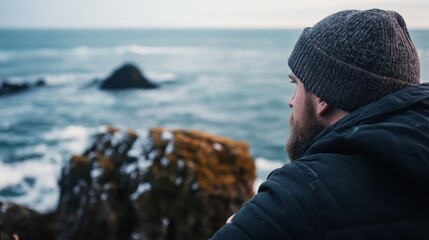 Aufkleber - A bearded man in a knit beanie gazes pensively at a dramatic ocean vista, rugged coastline rocks and turbulent waves in the background. : Generative AI