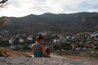 © Татьяна Толстая - mother and daughter sitting in the mountains and admiring the scenery, looking at the city at the foot of the mountains