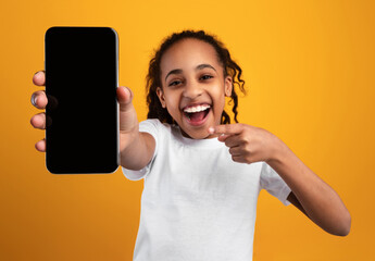 Poster - Excited Black Girl Pointing At Phone Blank Screen Showing Smartphone To Camera Recommending Application Over Yellow Studio Background. Great Mobile App For Cellphone Concept. Mockup