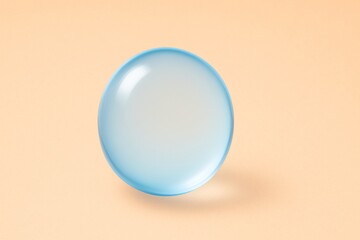 Poster - Glassy light blue sphere casting a soft shadow on a peach background, enhancing a minimalistic and elegant composition while providing ample copy space for creative use