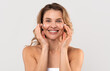 © Prostock-studio - Antiage Treatment. Beautiful Caucasian Woman Applying Moisturizing Cream On Face, Attractive Millennial Female Nourishing Skin While Standing Wrapped In Towel Over Light Studio Background, Copy Space