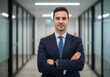 © Over View - Confident businessman in suit with arms crossed standing in office hallway looking at camera