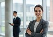 © Over View - Smiling businesswoman with crossed arms and colleague in office setting