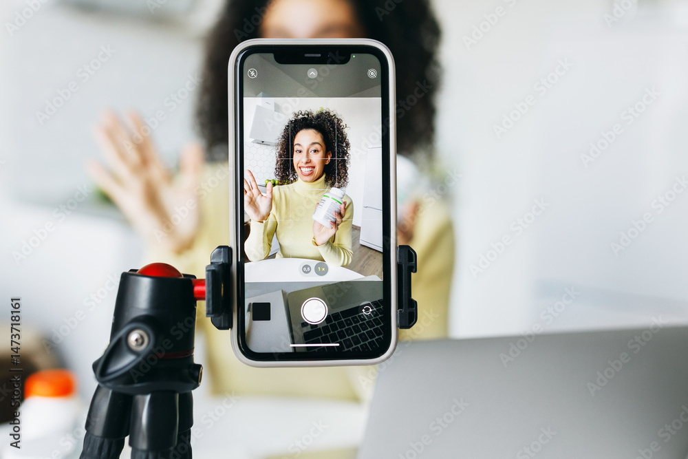 Selective focus on smartphone screen recording young health blogger or nutritionist advertising new food supplements, gesticulating holding bottle of vitamins and explaining its benefits for health