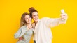© DMegias - Two happy young women taking a selfie with mobile phone on yellow background