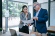 © Tj - Senior manager pointing at a document and explaining contract details to a young businesswoman in a modern office, analyzing financial report, discussing project results or planning new strategy