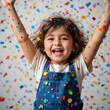 © Stacy - A joyful child celebrating with arms raised amidst colorful confetti.