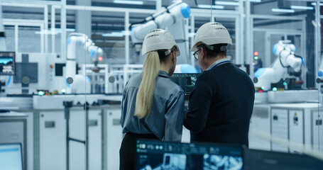 Fototapete - Female and Male Industrial Engineers Monitoring and Analyzing Conditions at a Modern Tech Electronics Factory with Automated Robot Arms Working with the Help of Artificial Intelligence Software