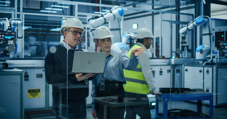 Fototapete - Female and Male Industrial Engineers Using Laptop Computer, Having a Conversation at a Modern Tech Electronics Factory with Automated Robot Arms Working with the Help of AI Software