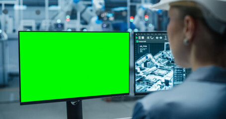 Fototapete - Female Industrial Specialist Working on a Desktop Computer with Green Screen Mock Up Display. Second Monitor Displaying Technical and Production Information About the Robotic Assembly Line