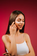 © Darius - Woman applying skincare product while smiling in front of pink backdrop