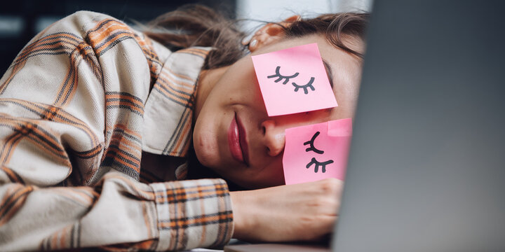 Close-up of woman sleeping on laptop, pink notes over eyes, depicting closed eyelids, showcasing exhaustion or burnout concept