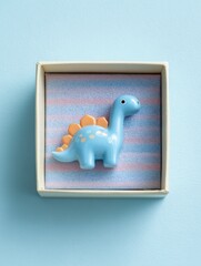 Poster - Colorful Gift Box With a Toy Dinosaur on a Pastel Blue Surface Providing Joy for Kids and Adding Playfulness to Childrens Celebrations