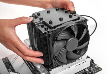 Poster - A person is installing a large black tower-style CPU cooler with a fan onto a motherboard during PC assembly.
