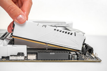Poster - A person is carefully inserting a white DDR RAM module into a motherboard slot during a desktop computer build.