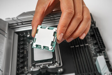 Poster - A person is carefully holding a computer processor above a motherboard socket, preparing to install it.