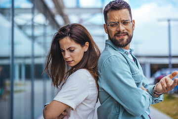 young couple facing disagreement standing back-to-back outdoors