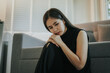 © Dara-Sroi - Depressed and unhappy Asian woman sits with anxiety on the sofa in her living room at home.