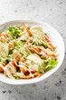 © pavel siamionov - Fresh vegetable salad with lettuce, cucumbers, tomatoes, croutons, and cashews, topped with creamy dressing and sesame seeds, served in a white bowl on a terrazzo countertop.