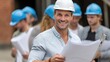 © lililia - Male architect in a white shirt and helmet holds blueprints and a level, smiling with team members on a construction site