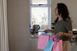 © wavebreak3 - Smiling woman holding colorful gift bags in kitchen, preparing for celebration