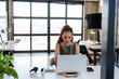 © Wavebreak Media - Woman in 30s working on laptop on wooden stand in loft office, using headphones and smartphone