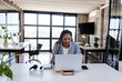 © Wavebreak Media - Young adult woman typing on laptop at open-plan office desk, with notebook, smartphone, headphones