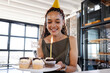 © Wavebreak Media - Mid-adult woman holding cupcakes with lit candle and glittery sign in loft, celebrating birthday