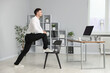 © New Africa - Handsome man exercising with chair in office