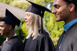 © wavebreak3 - Graduates in caps and gowns smiling outdoors, celebrating academic achievement