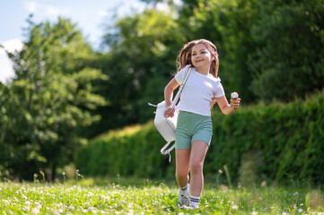 cute young child running while eating tasty cream dessert outdoors in park