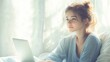 © hocine - Young woman sitting by the window with laptop, natural light illuminating her serene expression in cozy bedroom during morning time
