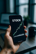 © ISSARA - Hand holding smartphone displaying rising stock chart, concept of online investment and trading